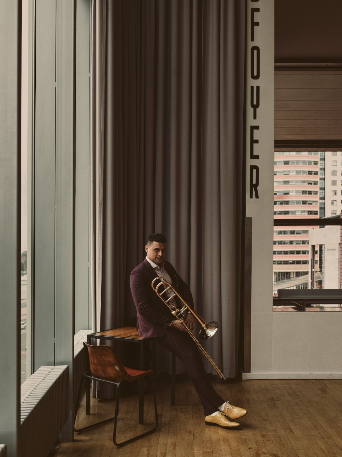Alejandro seated beside a window with his trombone
